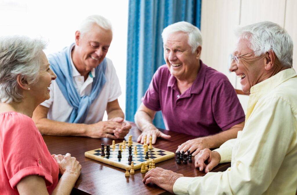 A group of older adults sitting at a table playing a game of chess in a senior living community