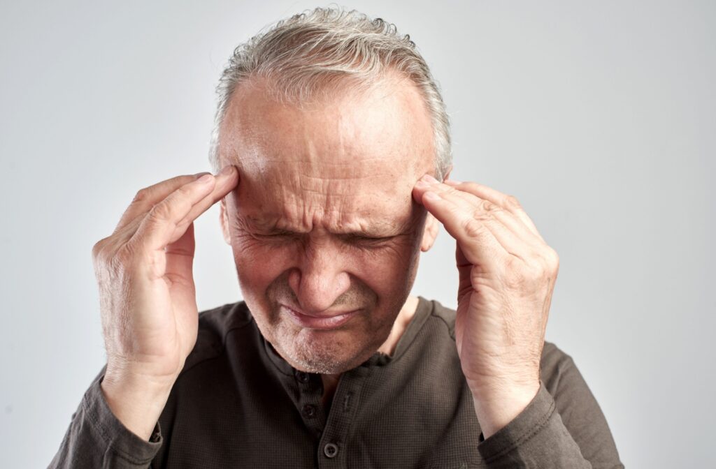 An elderly man touches the sides of his head with both hands as he tries to remember something.
